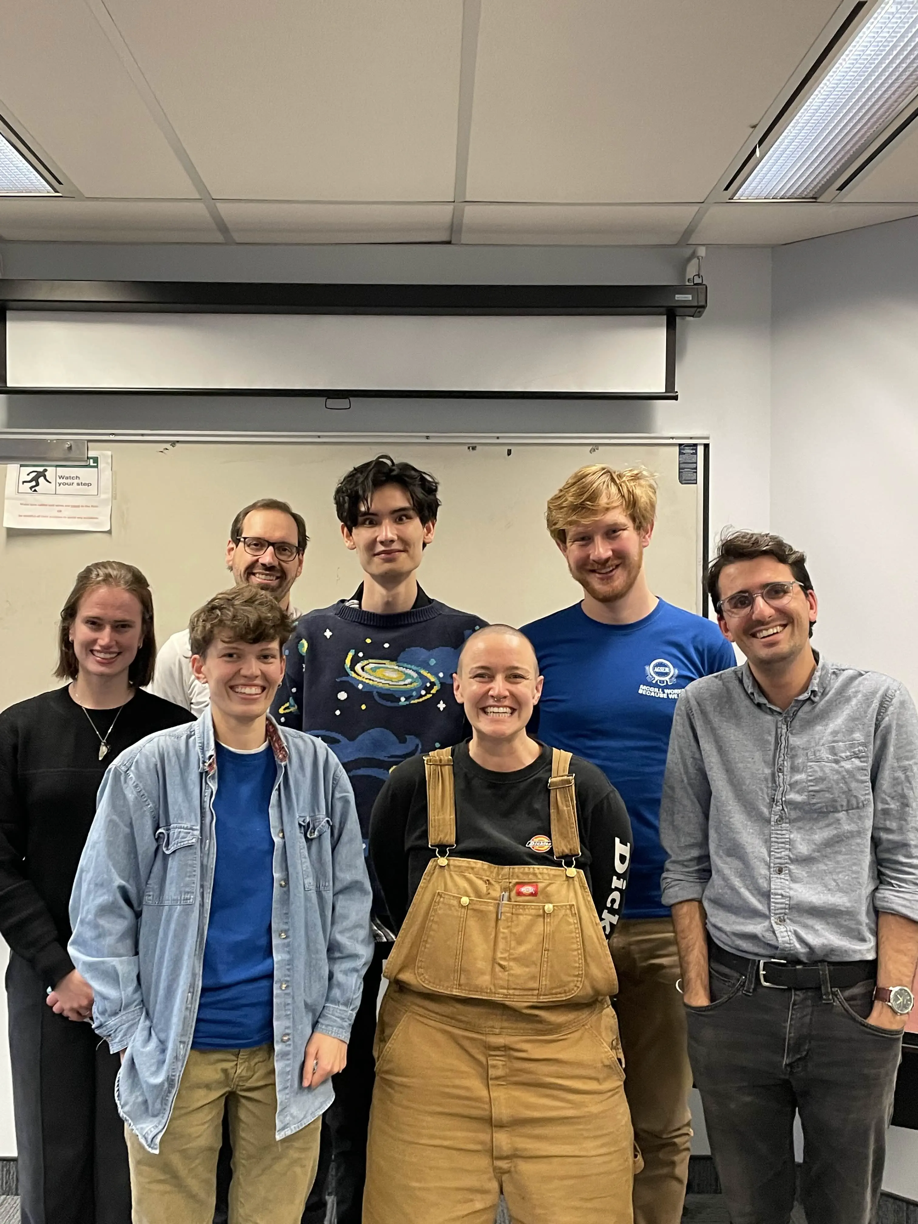 a group of seven people in a classroom, smiling at the camera.